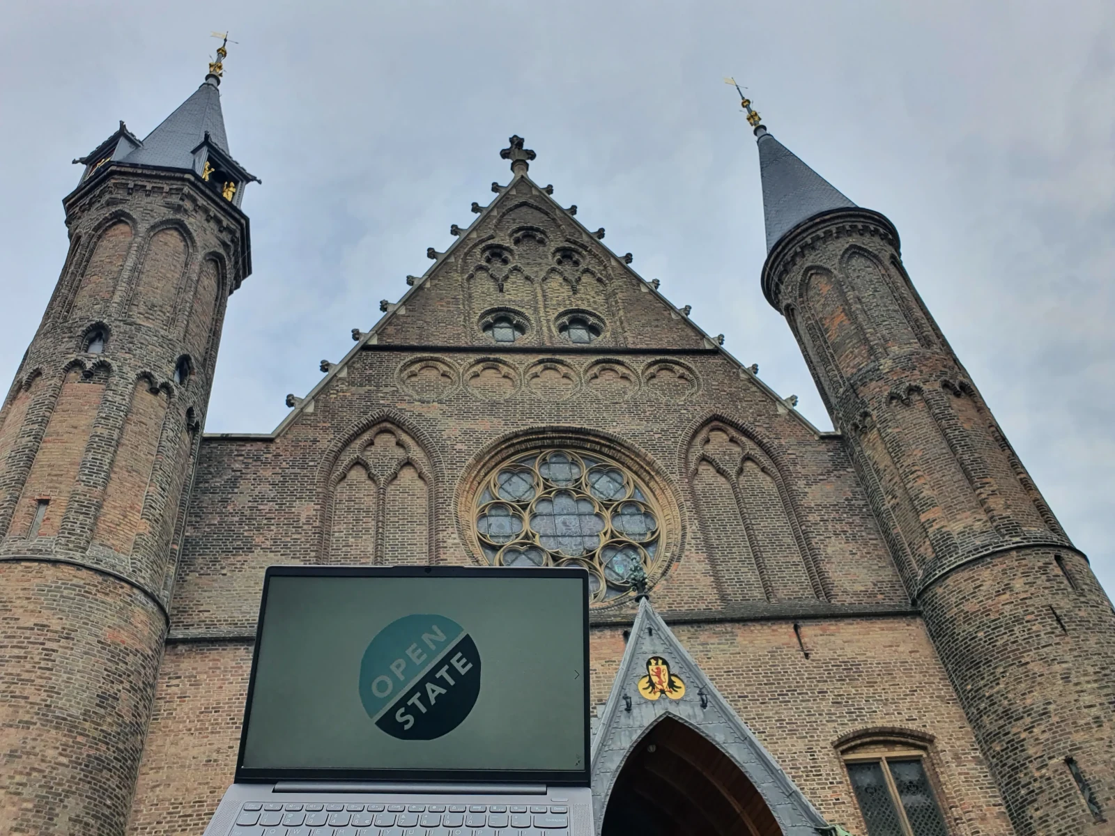 Foto van de voorkant van het Grafelijk kasteel op het Binnenhof met een laptop met daarop het logo van Open State Foundation